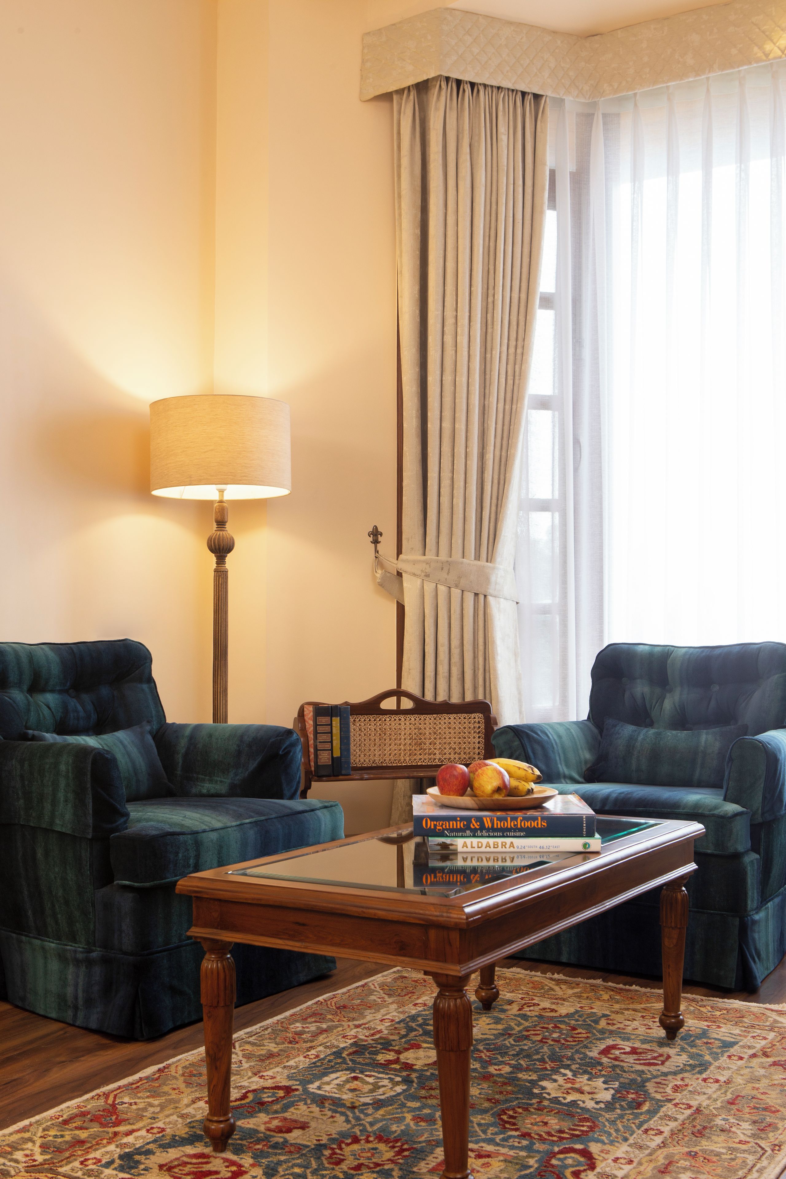 A living room with two blue armchairs, a wooden coffee table with books, a lamp, and a patterned rug.