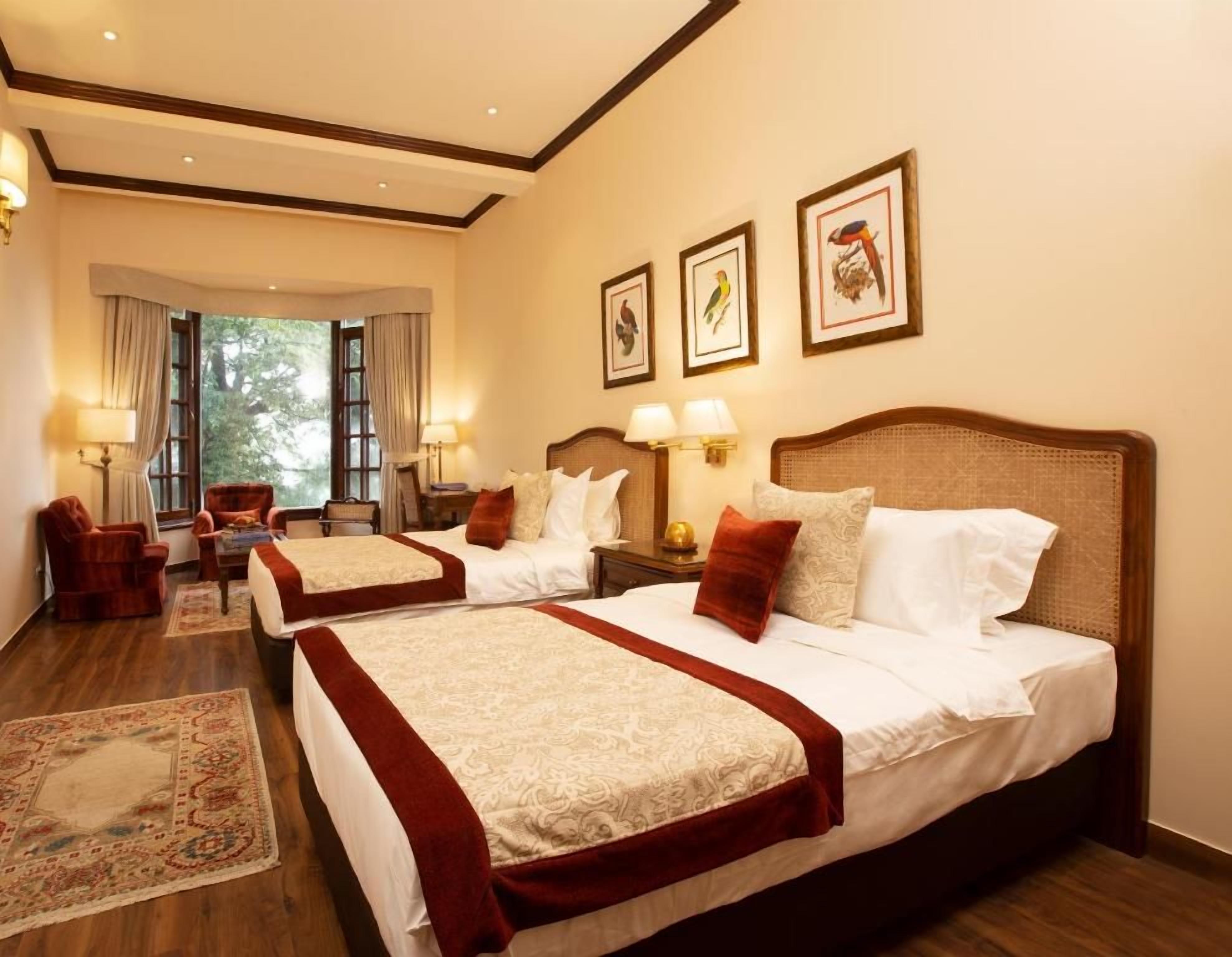 Habitación de hotel con dos camas, zona de estar con una silla, una mesa y vistas al exterior.