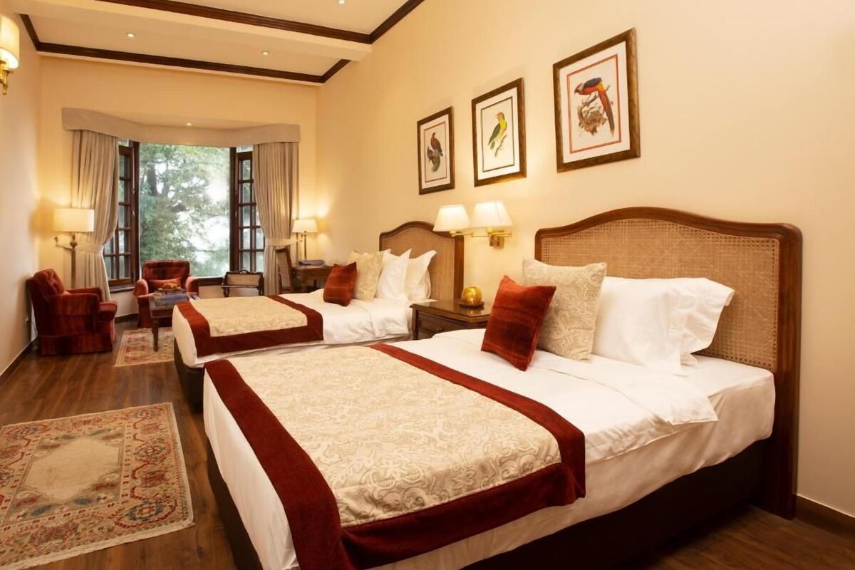 Habitación de hotel con dos camas, zona de estar con una silla, una mesa y vistas al exterior.