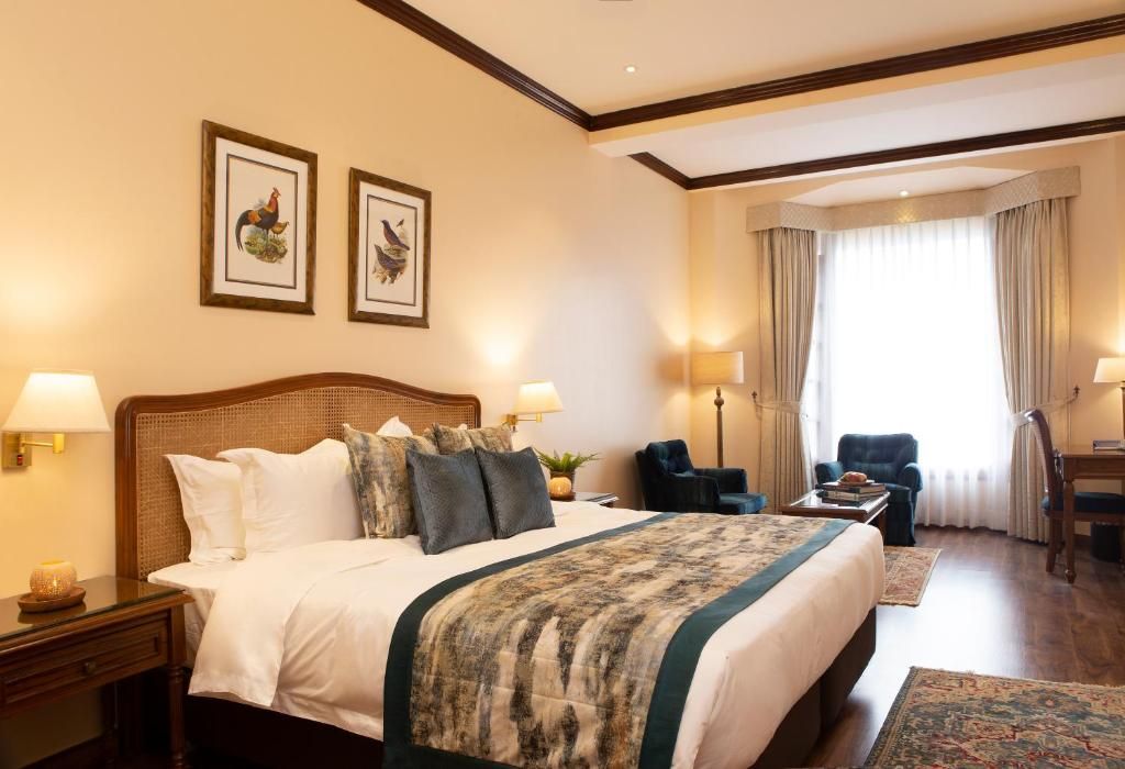 Ein Hotelzimmer mit einem großen Bett, zwei Wandleuchten, einem Sessel, einem Schreibtisch und einem Fenster mit Vorhängen.