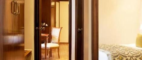 A hotel hallway with a wooden floor, a bed with patterned bedding, and a chair in the background.