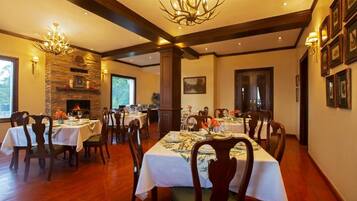 Un comedor con varias mesas dispuestas para una comida, una chimenea de piedra y un candelabro.
