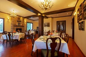 Un comedor con varias mesas dispuestas para una comida, una chimenea de piedra y un candelabro.