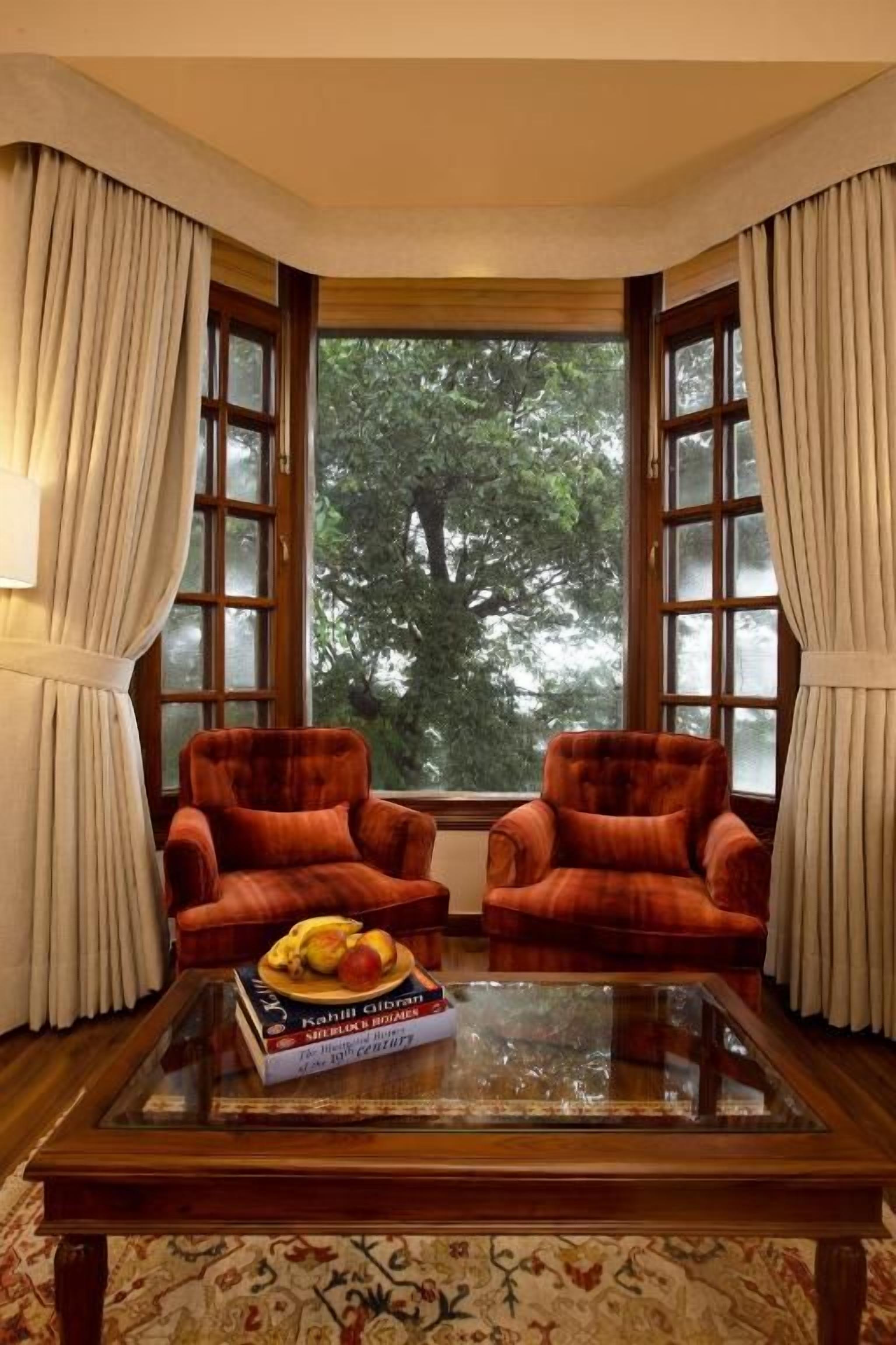 A room with two armchairs, a glass-top coffee table, and a view through large windows.