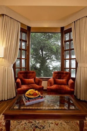 A room with two armchairs, a glass-top coffee table, and a view through large windows.