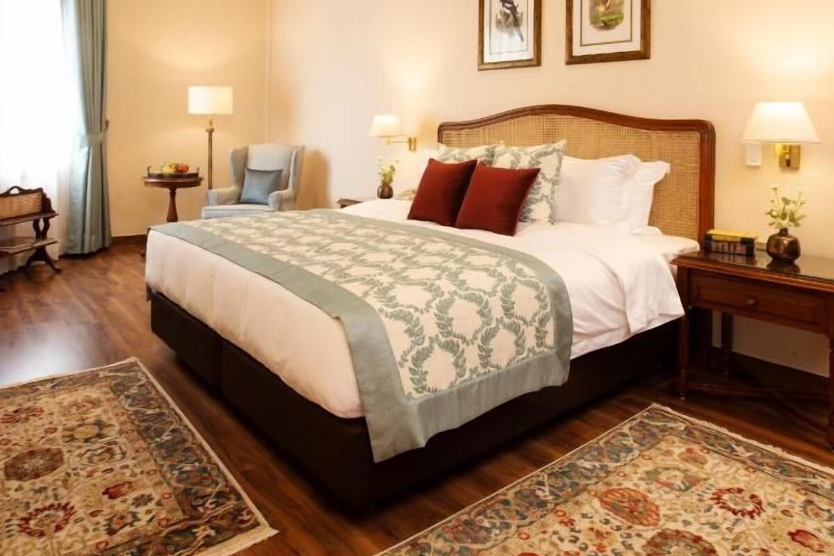 Una habitación de hotel con una cama grande, un ventilador de techo, dos lámparas de pared y una mesita de noche con lámpara.