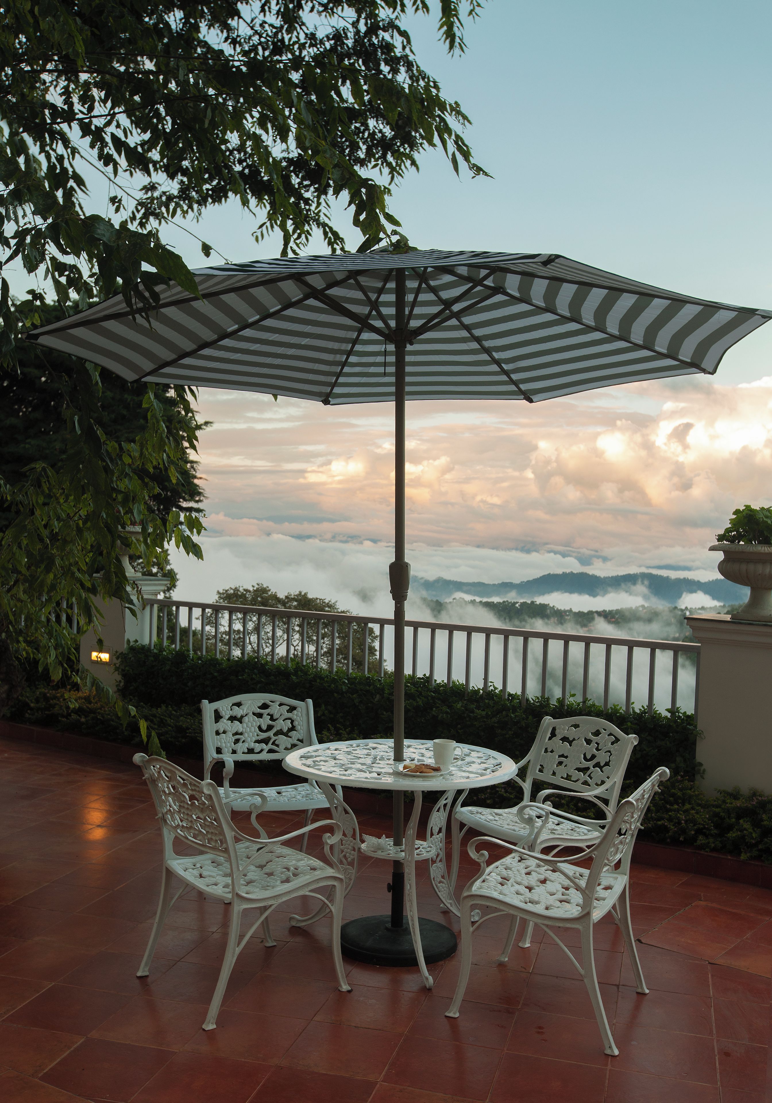 A patio with a round table and four chairs, an umbrella, and a view of clouds and mountains.