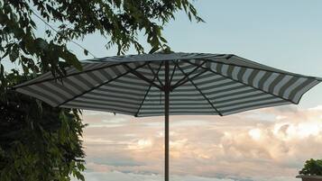 A patio with a round table and four chairs, an umbrella, and a view of clouds and mountains.