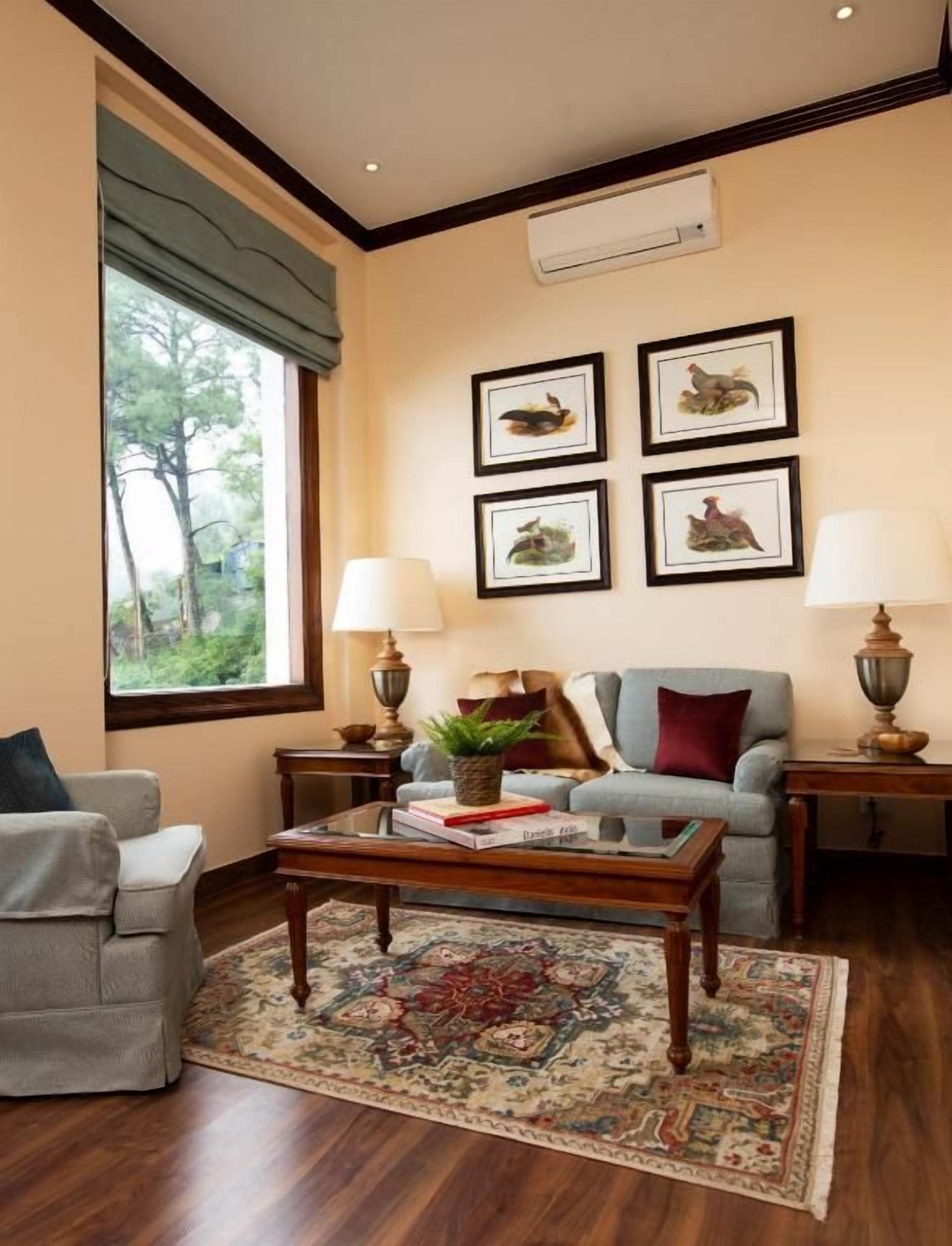 A living room with a sofa, armchairs, a coffee table, and a rug. There are framed pictures on the wall and two lamps on side tables.