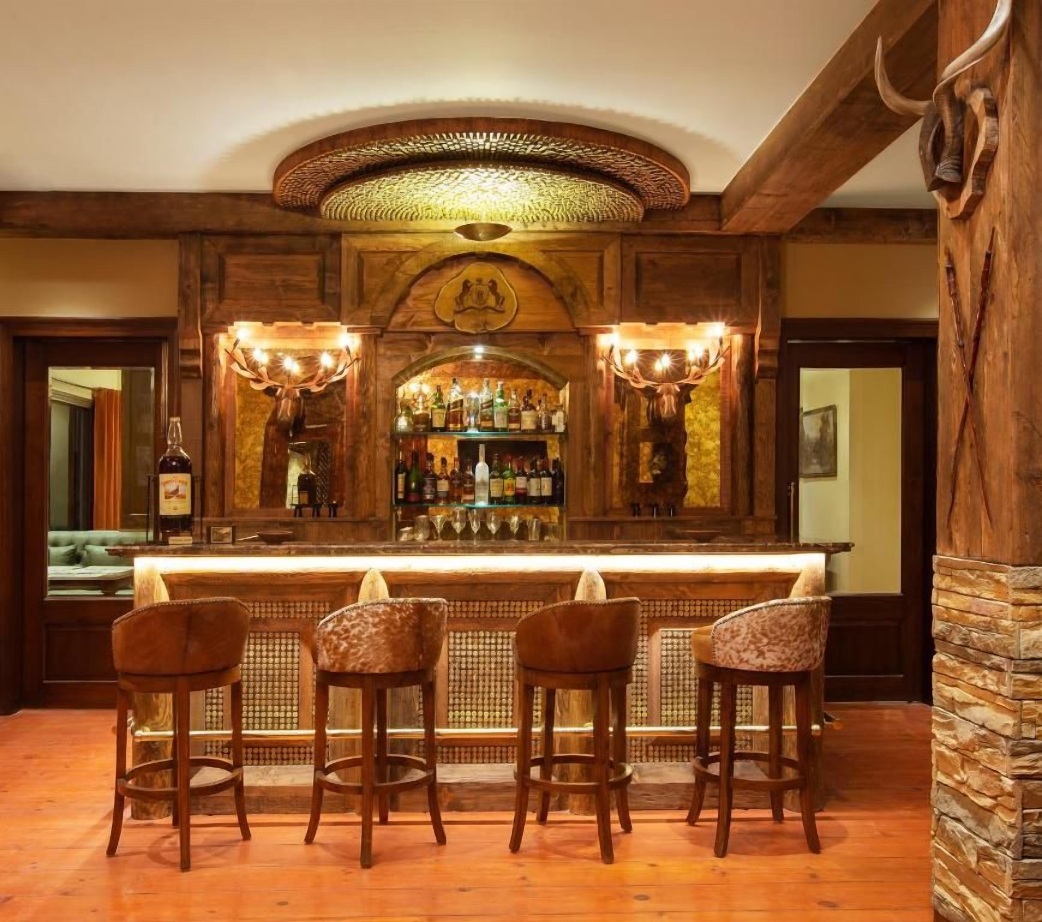 Eine Bar mit einer Holztheke, vier Barhocker und einer Auswahl an Flaschen.
