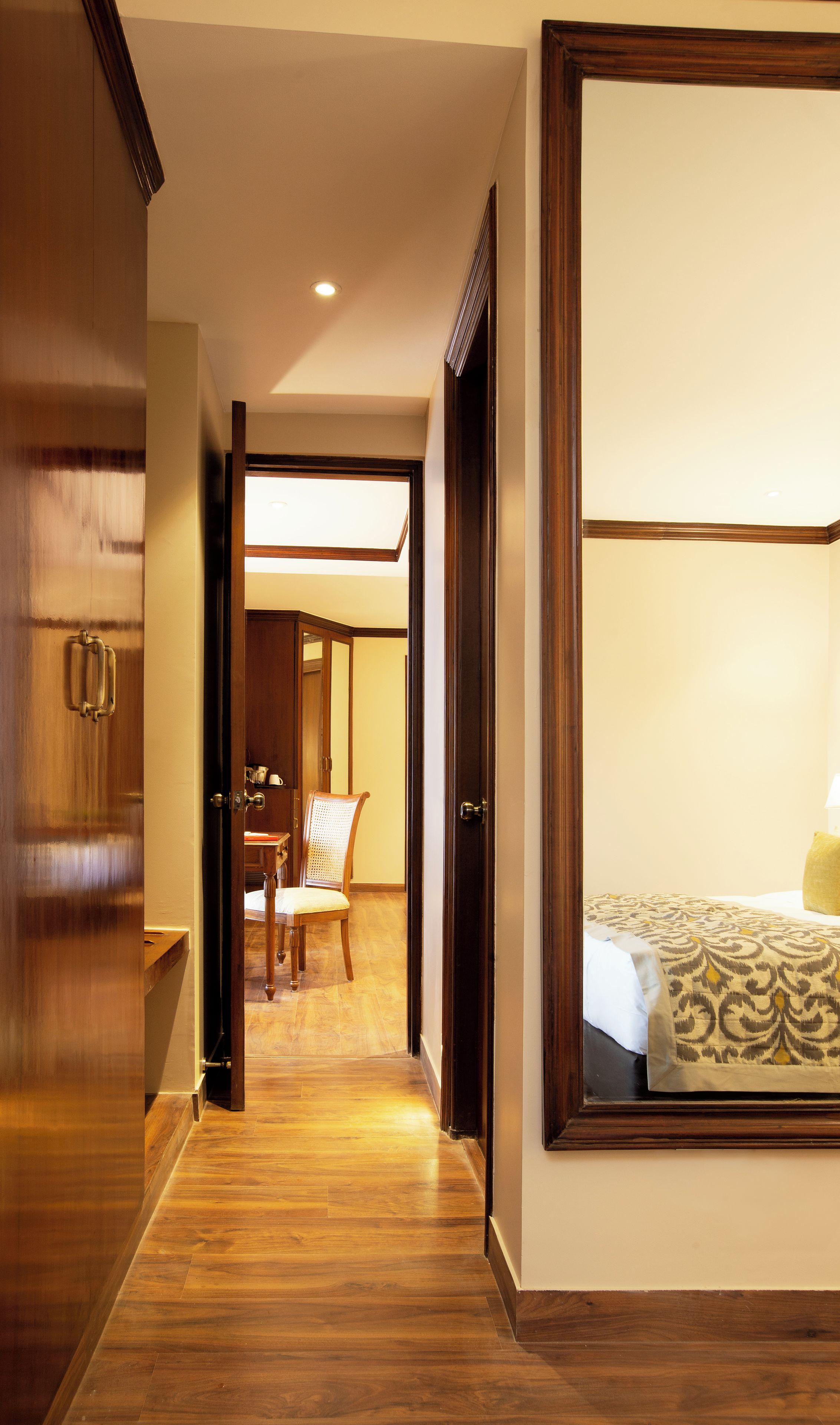 A hotel room with a wooden floor, a bed with a patterned bedspread, and a chair in the background.