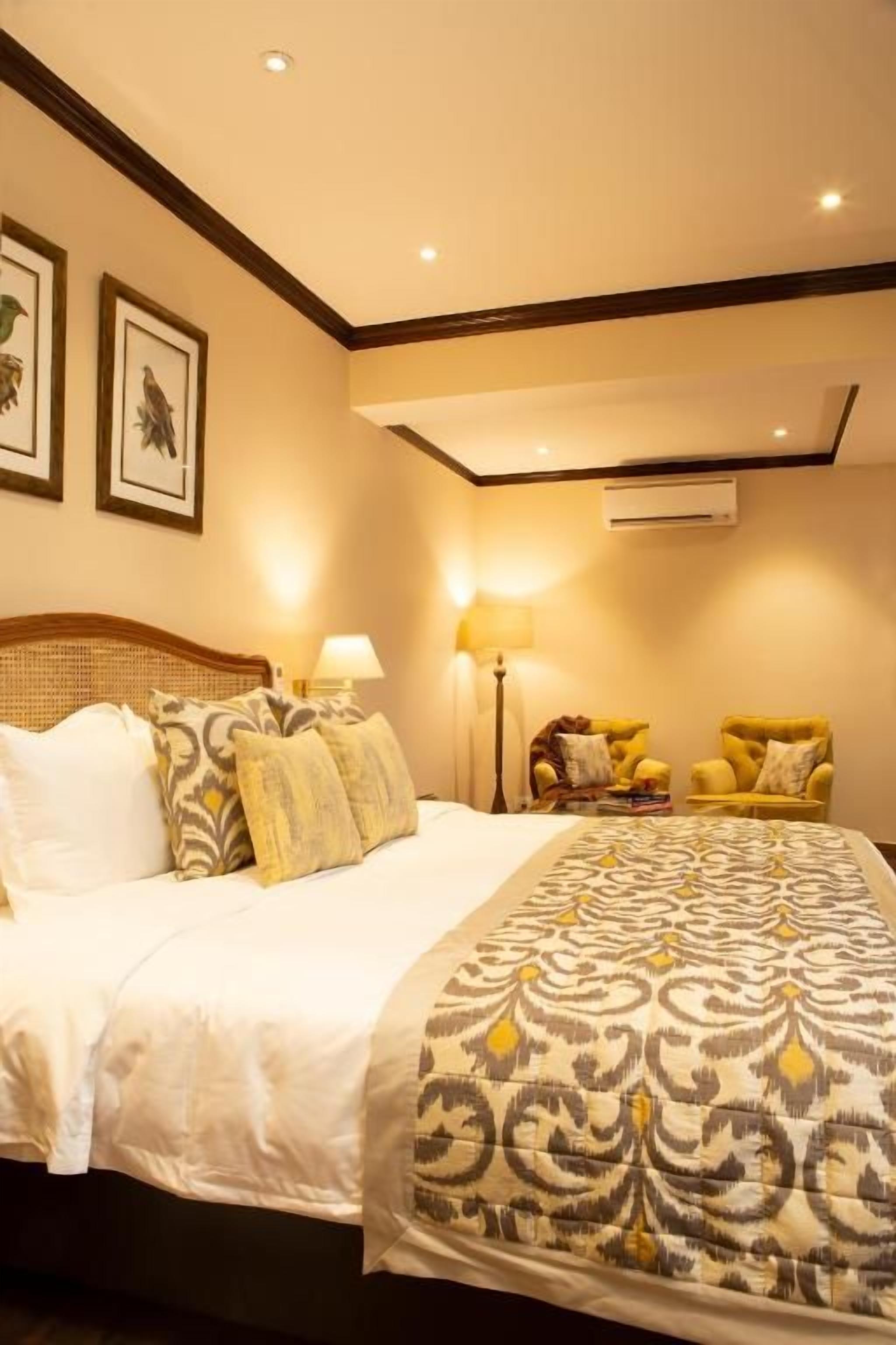 A hotel room with a large bed, two bedside lamps, a chair, and a wall-mounted air conditioner.
