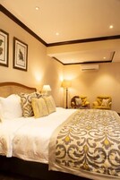 A hotel room with a large bed, two bedside lamps, a chair, and a wall-mounted air conditioner.