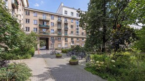 Un immeuble à plusieurs étages doté d’une entrée centrale, entouré de verdure et bordé d’un chemin piétonnier dallé.