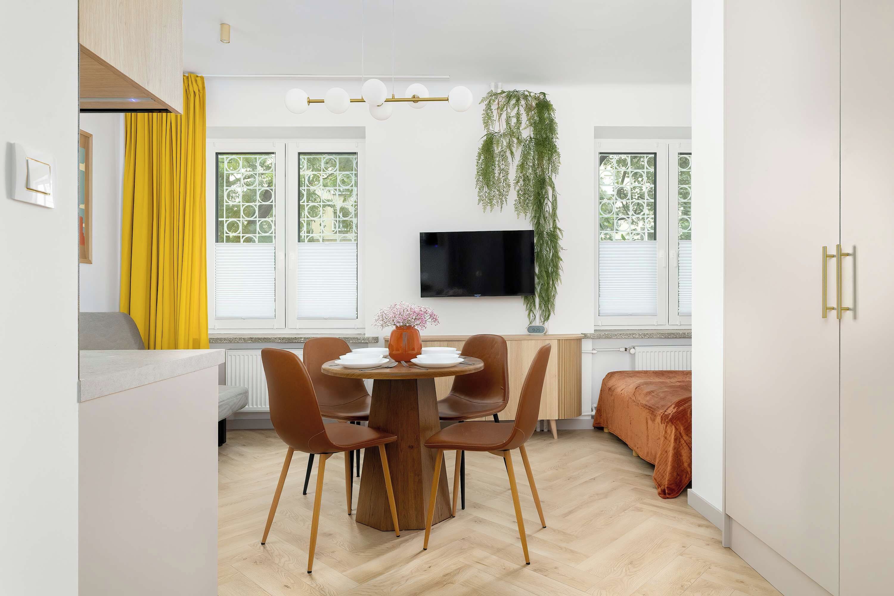 Une cuisine moderne avec un coin repas, un téléviseur à écran plat fixé au mur et une plante suspendue.