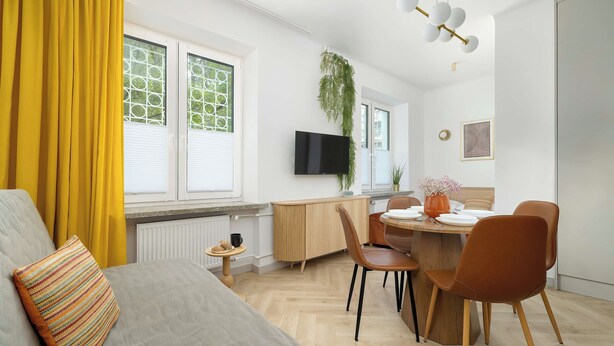 Un salon moderne comprenant un canapé, une table à manger avec des chaises, un téléviseur à écran plat et une grande fenêtre équipée de stores.