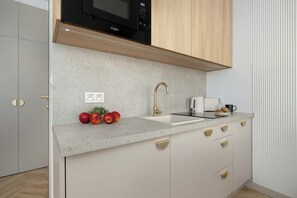Una cocina compacta con microondas, lavamanos y una encimera con manzanas.