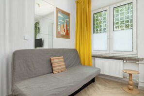 Una sala de estar moderna con un sofá gris, una cortina amarilla y un ventanal con diseño geométrico.
