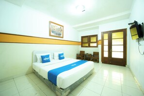 A hotel room with a bed, a desk, a chair, a television, and a door with frosted glass panels.