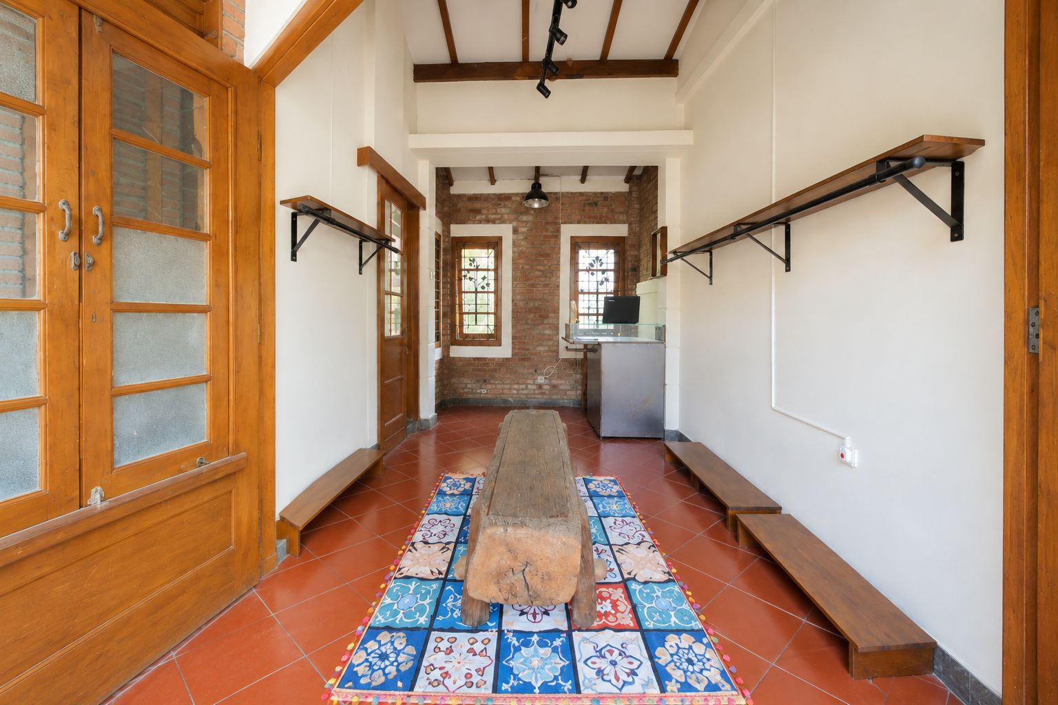 A hallway with a wooden bench, tiled floor, and a brick wall.