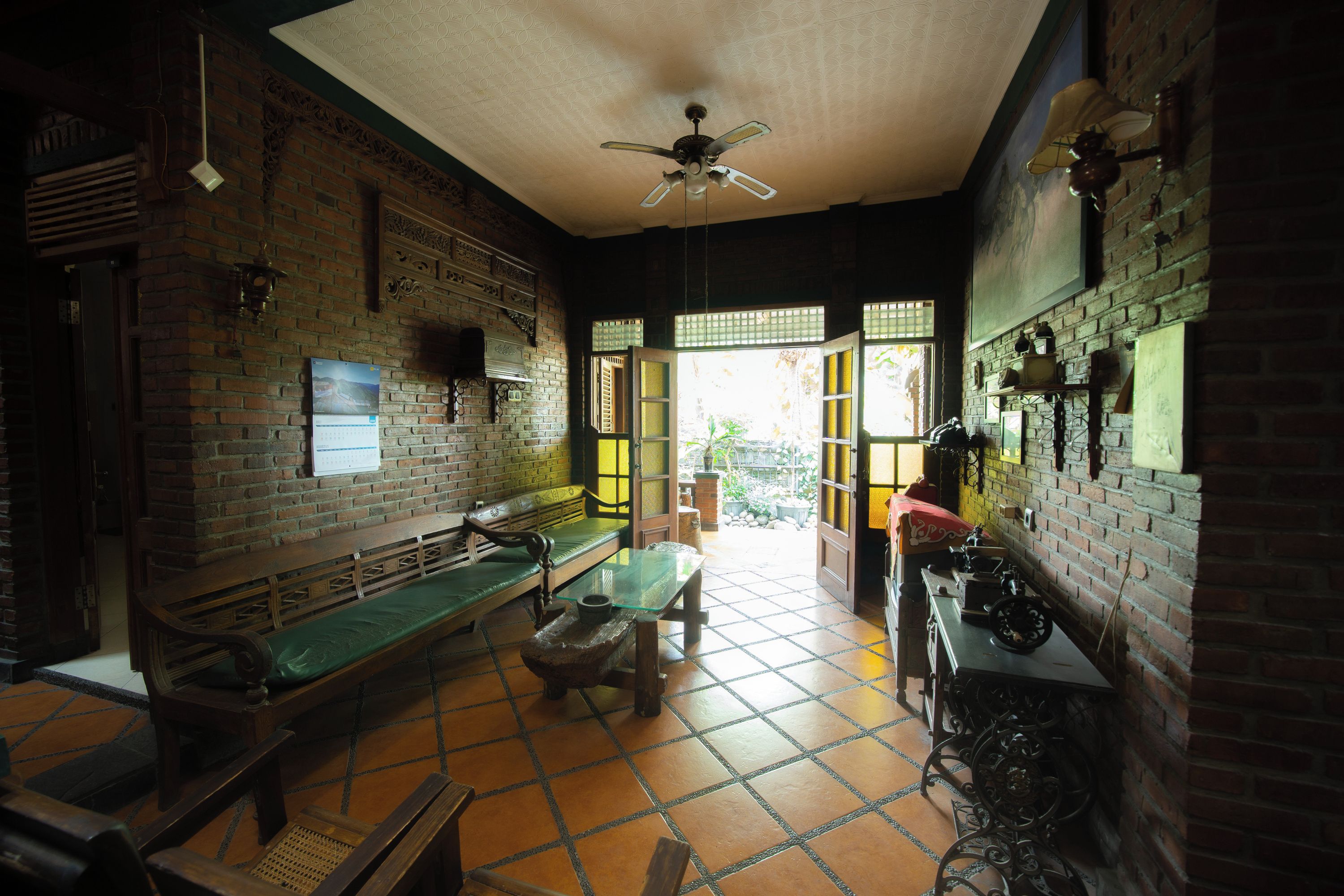 Una habitación con pared de ladrillo, ventilador de techo, un banco, una mesa y una ventana.