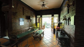 Una habitación con pared de ladrillo, ventilador de techo, un banco, una mesa y una ventana.
