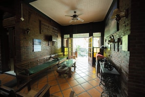 Una habitación con pared de ladrillo, ventilador de techo, un banco, una mesa y una ventana.