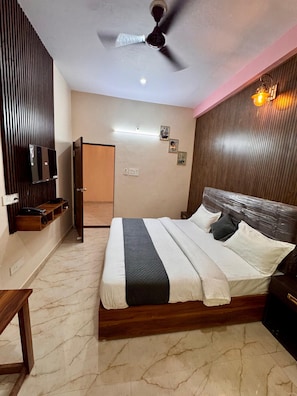 Un dormitorio con cama, ventilador de techo, televisor montado y mesita de noche.