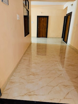 Un pasillo con piso de mármol, puertas de madera y pared de color claro.