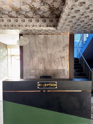 A reception desk with a 'RECEPTION' sign, a marble wall, and a staircase with a metal railing.