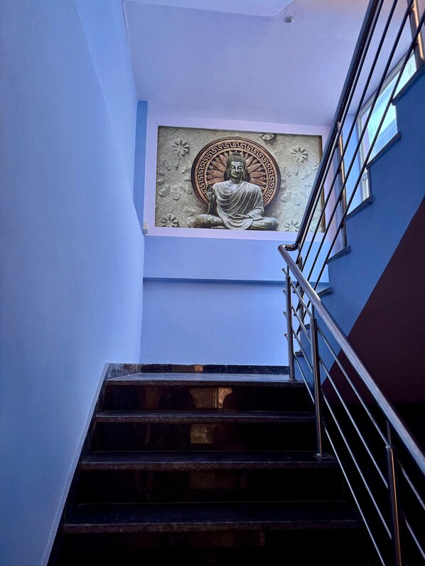 A staircase with a metal railing leading to a room with a Buddha statue on the wall.