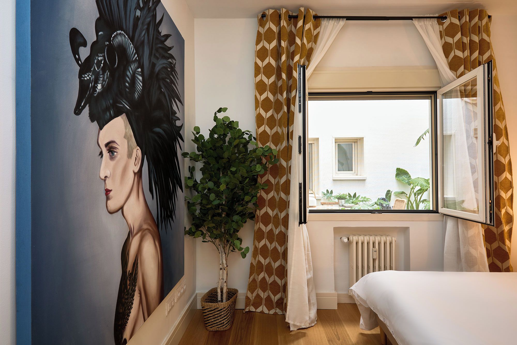 A bedroom with a bed, a window with curtains, a radiator, and a wall with a painting.