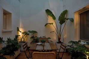 Eine Terrassenfläche mit einem Holztisch und Stühlen, umgeben von Kübelpflanzen und einer weißen Wand.