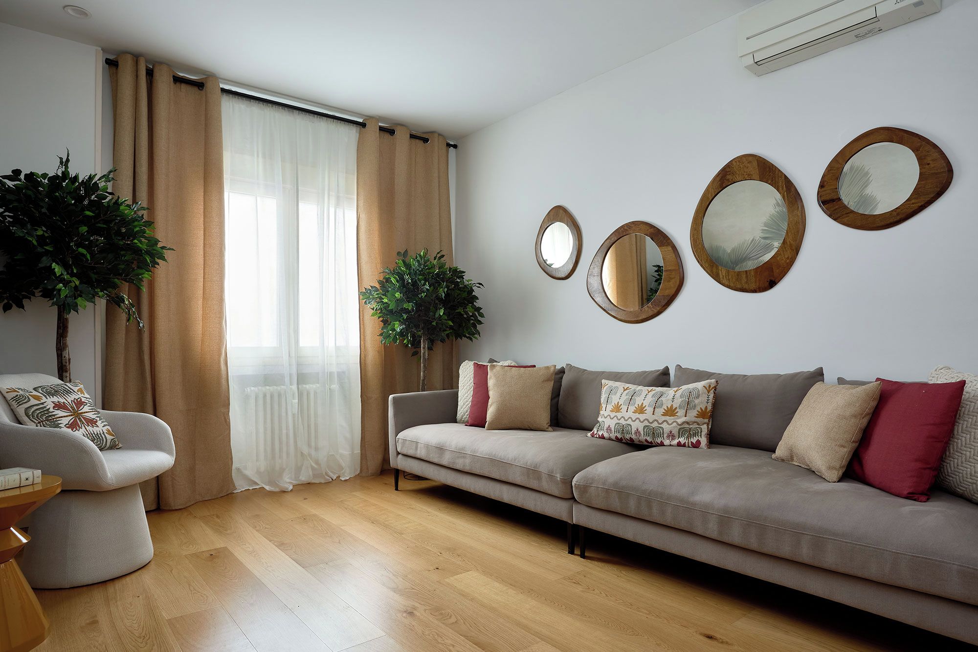 A living room with a sofa, two side tables, a potted plant, and a window with curtains.