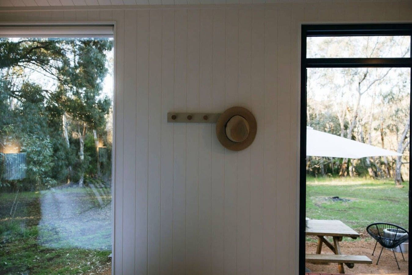 A room with a wooden door, a hat hanging on the wall, and a view of a garden with a picnic table and umbrella.