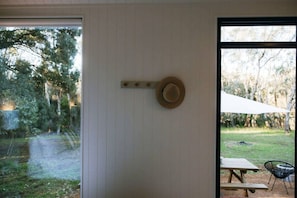 A room with a wooden door, a hat hanging on the wall, and a view of a garden with a picnic table and umbrella.