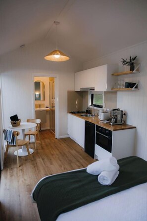 A compact hotel room with a kitchenette, a dining area, and a bed with towels.