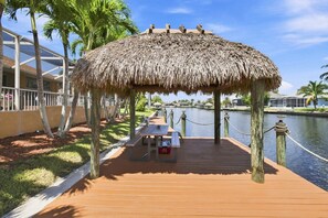 A wooden dock with a thatched-roof pavilion, palm trees, and a body of water. - Villa American Dream — Luxury Waterfront Villa in Cape Coral with Gulf access (Cape Coral)