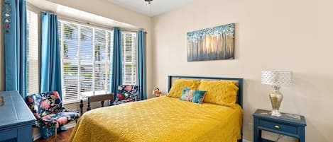 Un dormitorio con cama, escritorio, silla, ventilador de techo y ventana con cortinas.
