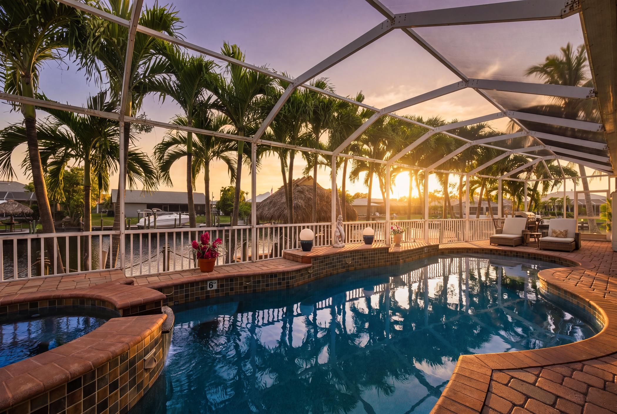 A swimming pool with a sunken seating area, surrounded by palm trees and a covered patio.