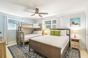 Ein Schlafzimmer mit einem großen Bett, zwei kleineren Betten, einem Deckenventilator, einem Nachttisch mit Lampe und einem Fenster mit Jalousien.
