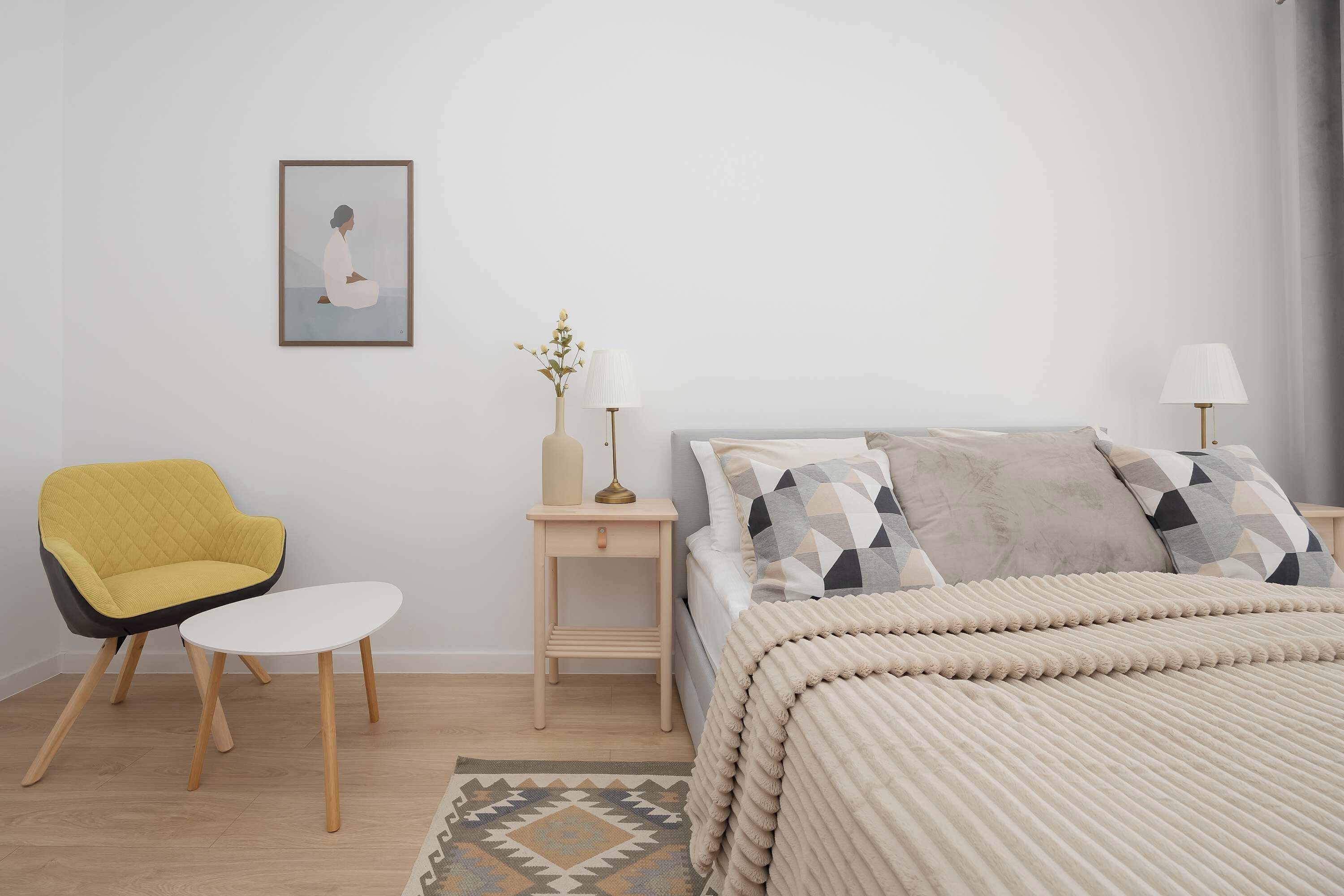 A bedroom with a bed, a chair, a bedside table, a lamp, and a picture on the wall.
