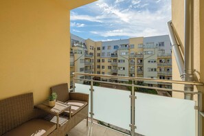 A balcony with a wicker sofa and a small table, overlooking a multi-story residential building. - Comfortable Apartment with a Balcony | Parking (Warszawa)