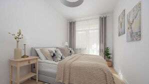 Ein Schlafzimmer mit Bett, Nachttisch, Lampe, Vorhängen und Wandbildern.