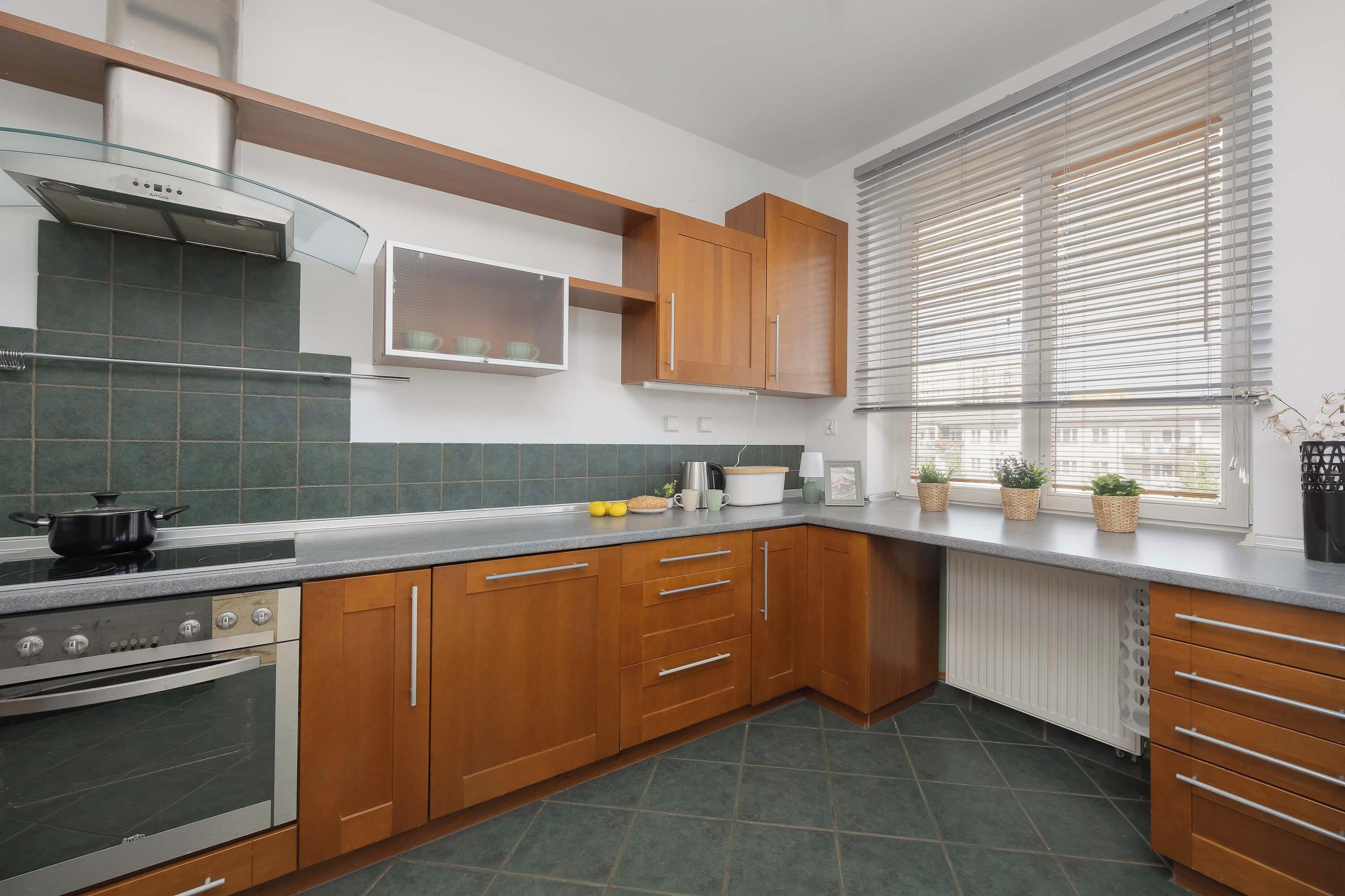 A modern kitchen with wooden cabinets, a stove, and a window with blinds.