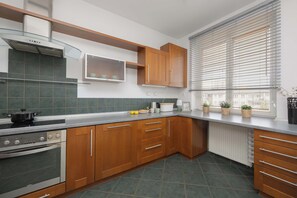 A modern kitchen with wooden cabinets, a stove, and a window with blinds.