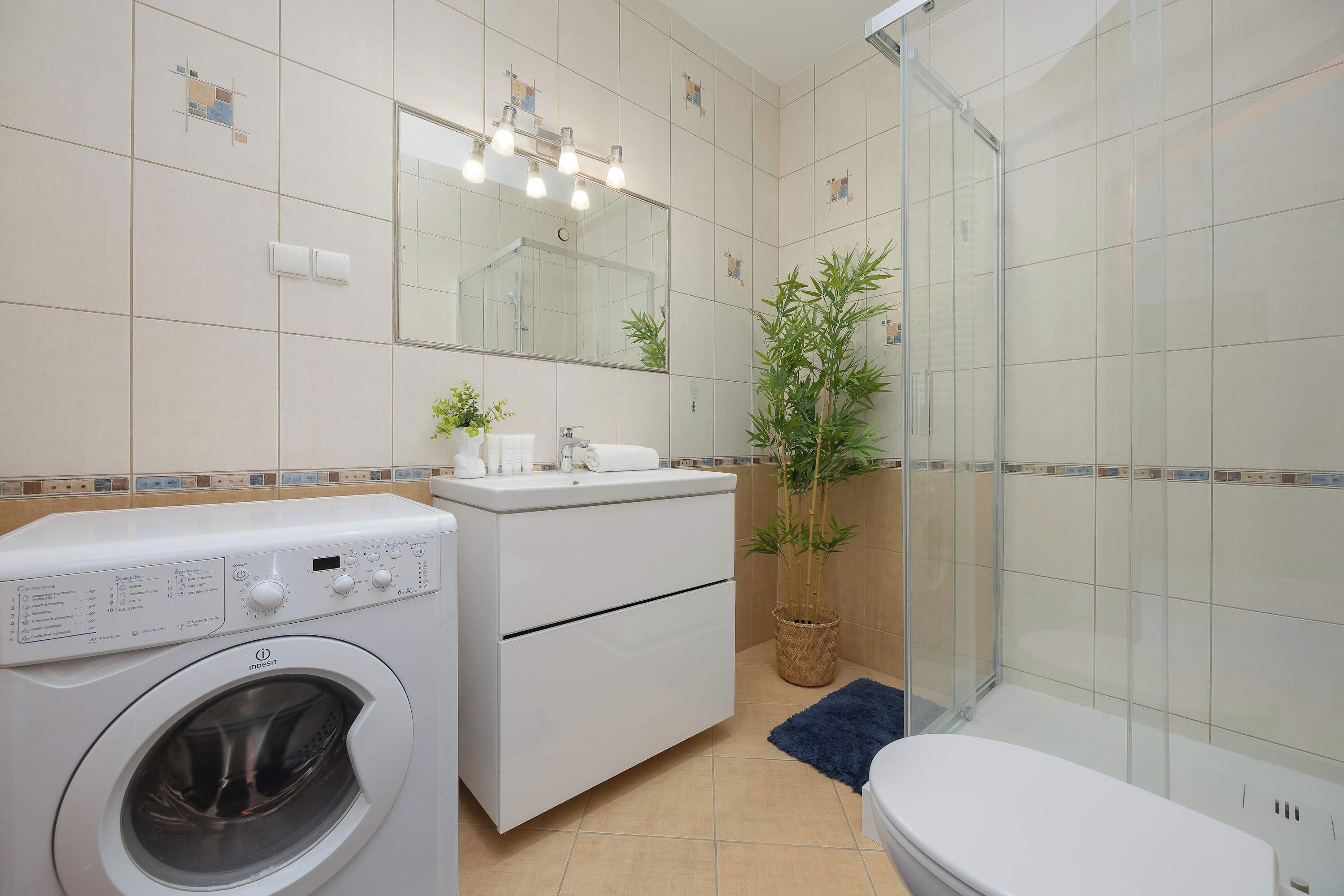 Une salle de bain moderne équipée d’un lave-linge, d’un évier, d’un miroir et d’un espace douche.