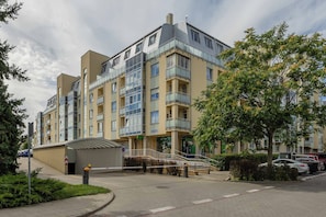 Un edificio residencial de varios pisos con balcones, entrada protegida por un portón y un pequeño estacionamiento.