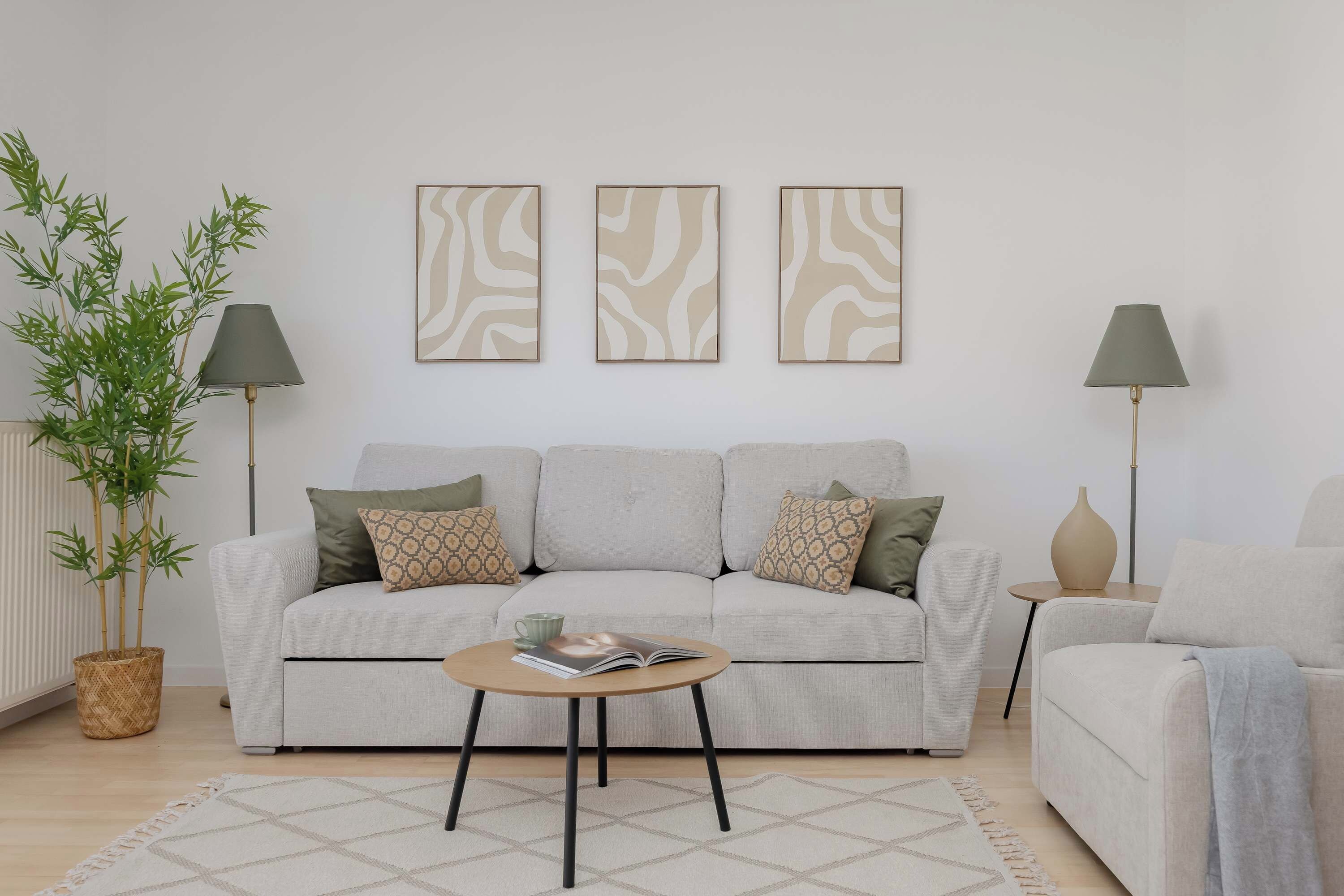 Uma sala de estar com sofá, duas mesinhas laterais, uma mesa de centro e um vaso com planta.