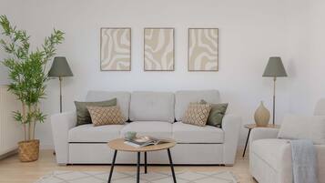Uma sala de estar com sofá, duas mesinhas laterais, uma mesa de centro e um vaso com planta.